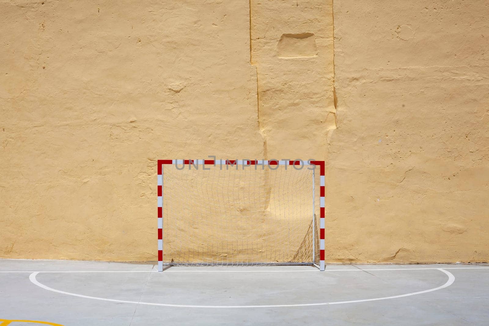 Soccer ball and goal with net against plastered wall background. Football at school yard scenery