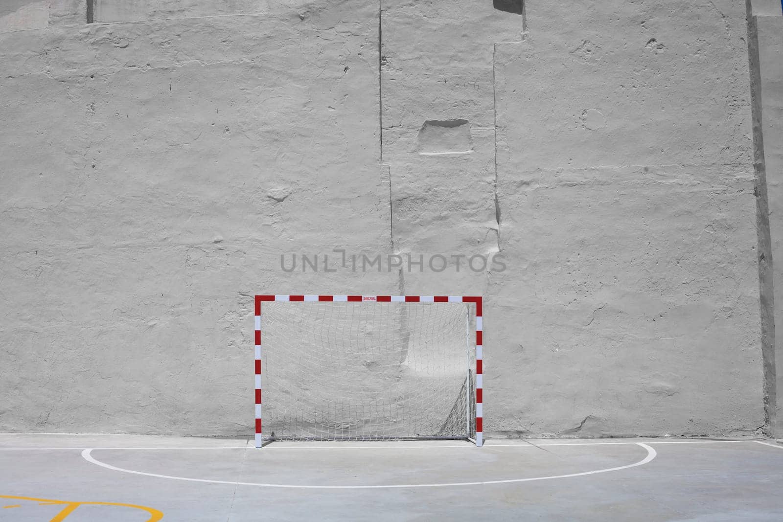 Soccer ball and goal with net against plastered wall background. Football at school yard scenery