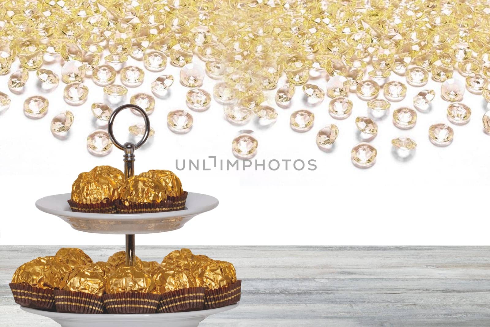 Pastries, desserts and sweets. Chocolate candies wrapped in golden foil on a two-storey etagere on a wooden table. Abstract bright background. Space for design.
