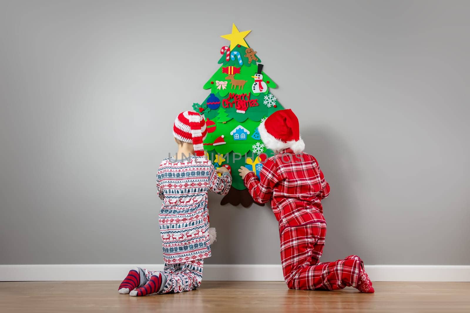 Children decorating wall of the room by green toy fir Christmas tree. Concept of the Xmas and New Year.