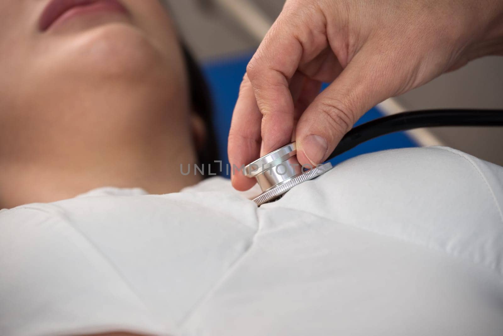 Cropped image of female doctor hand using medical stethoscope for checking heartbeat rate of woman patient on bed in hospital . Healthcare and insurance concept