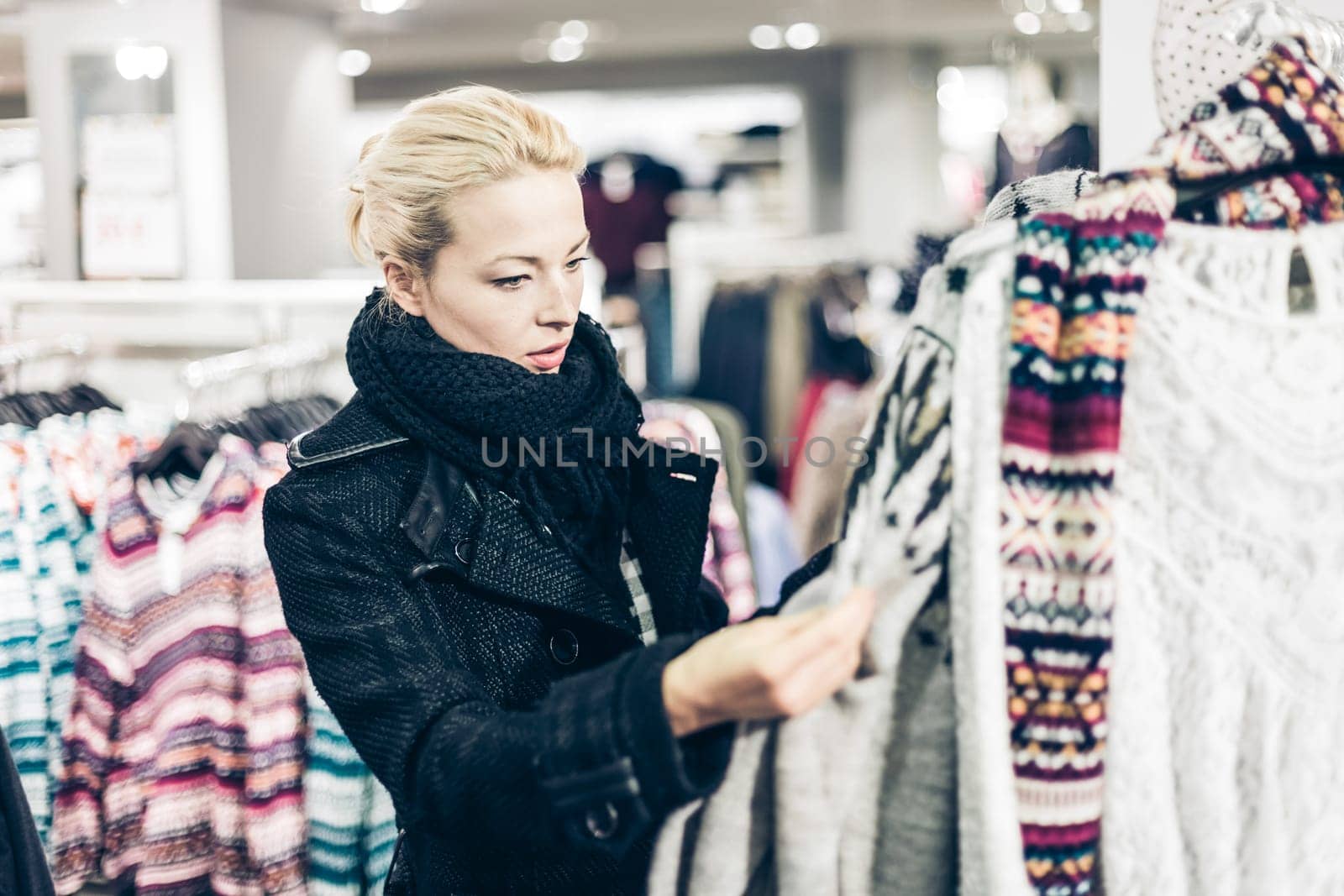 Woman shopping clothes. Shopper looking at clothing indoors in store. Beautiful blonde caucasian female model.