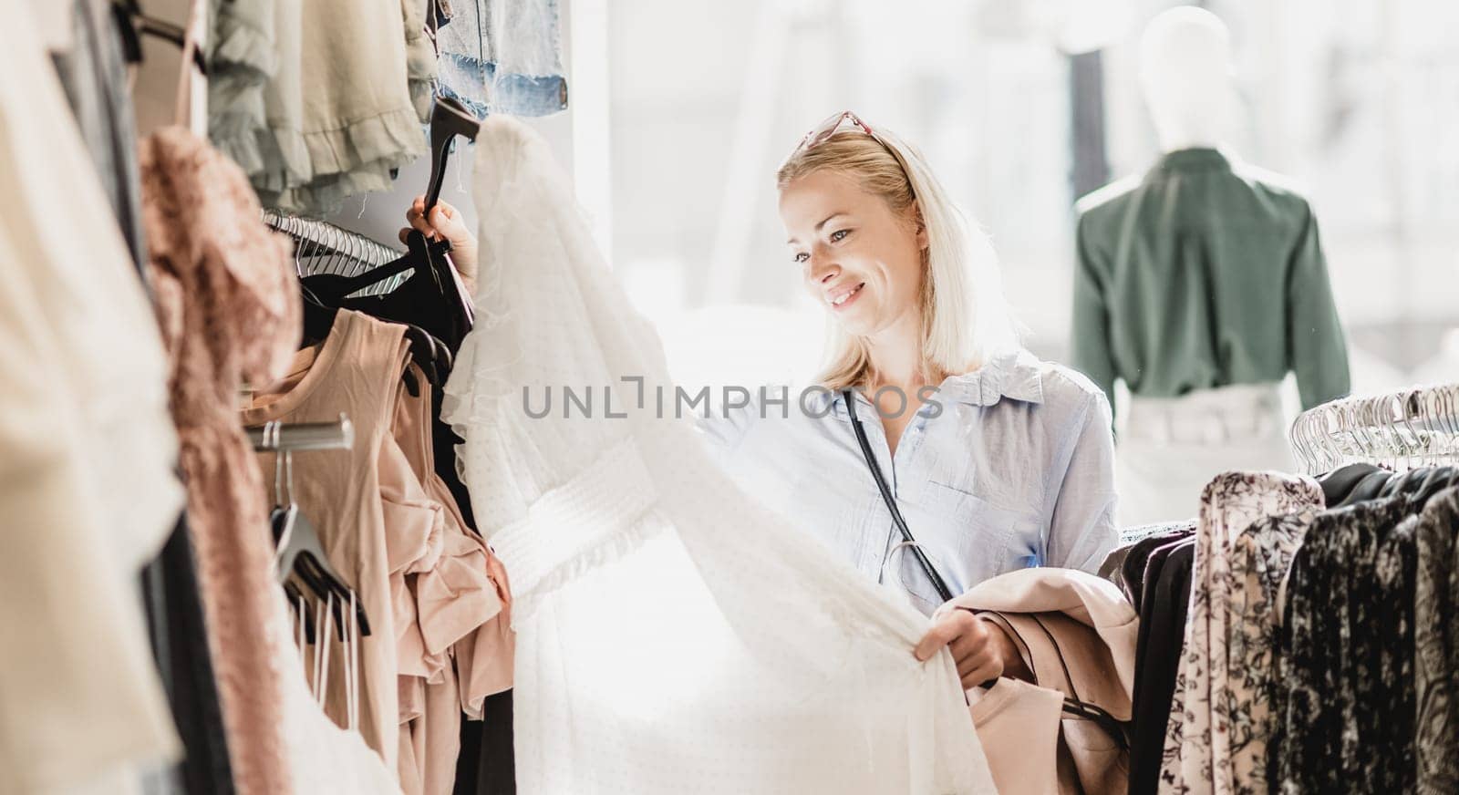 Woman shopping clothes. Female shopper looking at fashionable clothes indoors in clothing store.