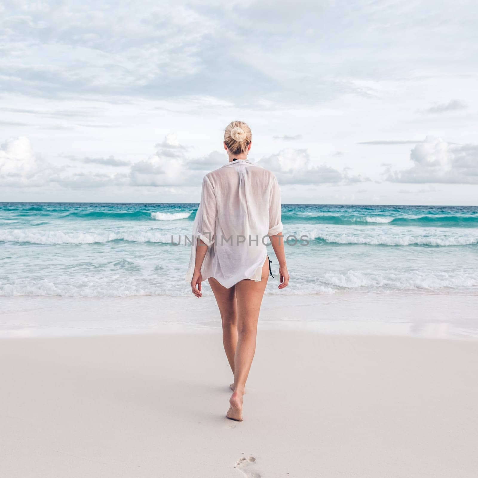 Woman wearing white loose tunic over bikini on Mahe Island, Seychelles. Summer vacations on picture perfect tropical beach concept.