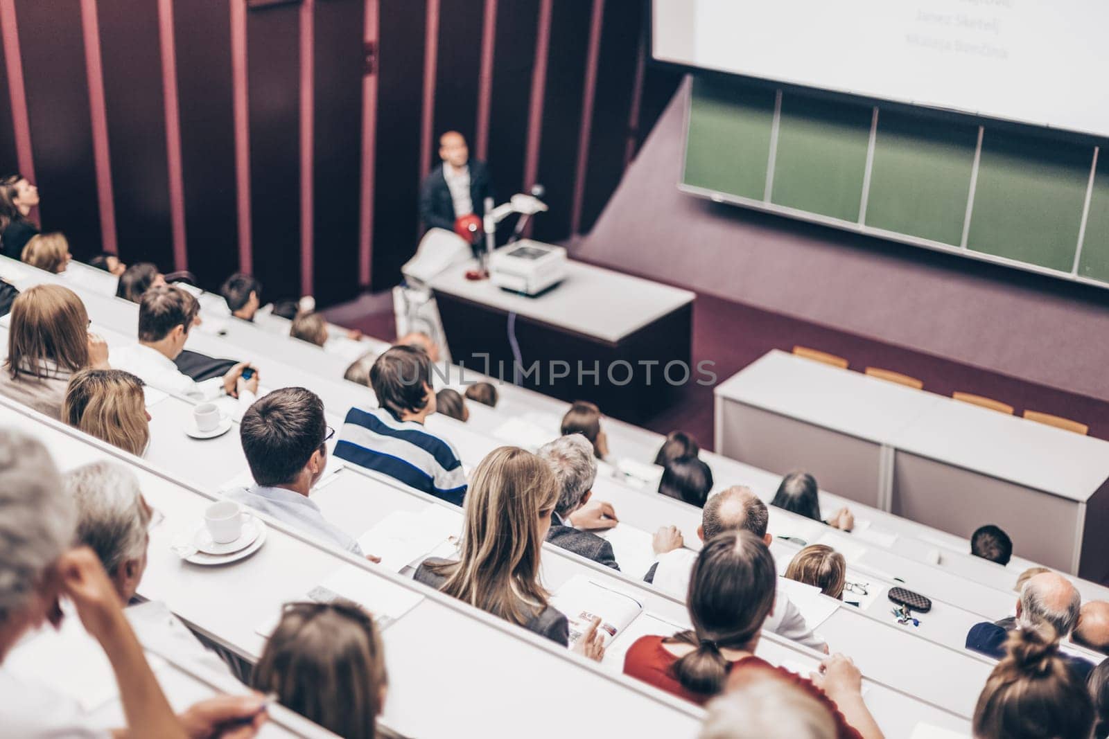Lecturer at university. Healthcare expert giving a talk to medical faculty professors. Participants listening to lecture and making notes.
