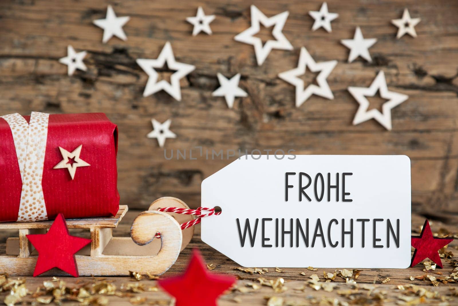 Wooden Sled With Red Gift And Rustic Christmas Background With Label With German Text Frohe Weihnachten, Which Means Merry Christmas In English