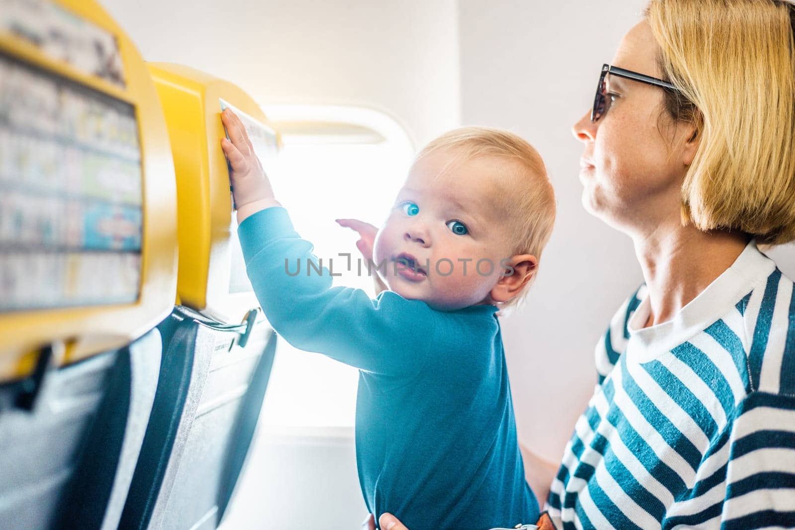 Mom and child flying by plane. Mother holding and playing with her infant baby boy child in her lap during economy comercial flight. Concept photo of air travel with baby. Real people
