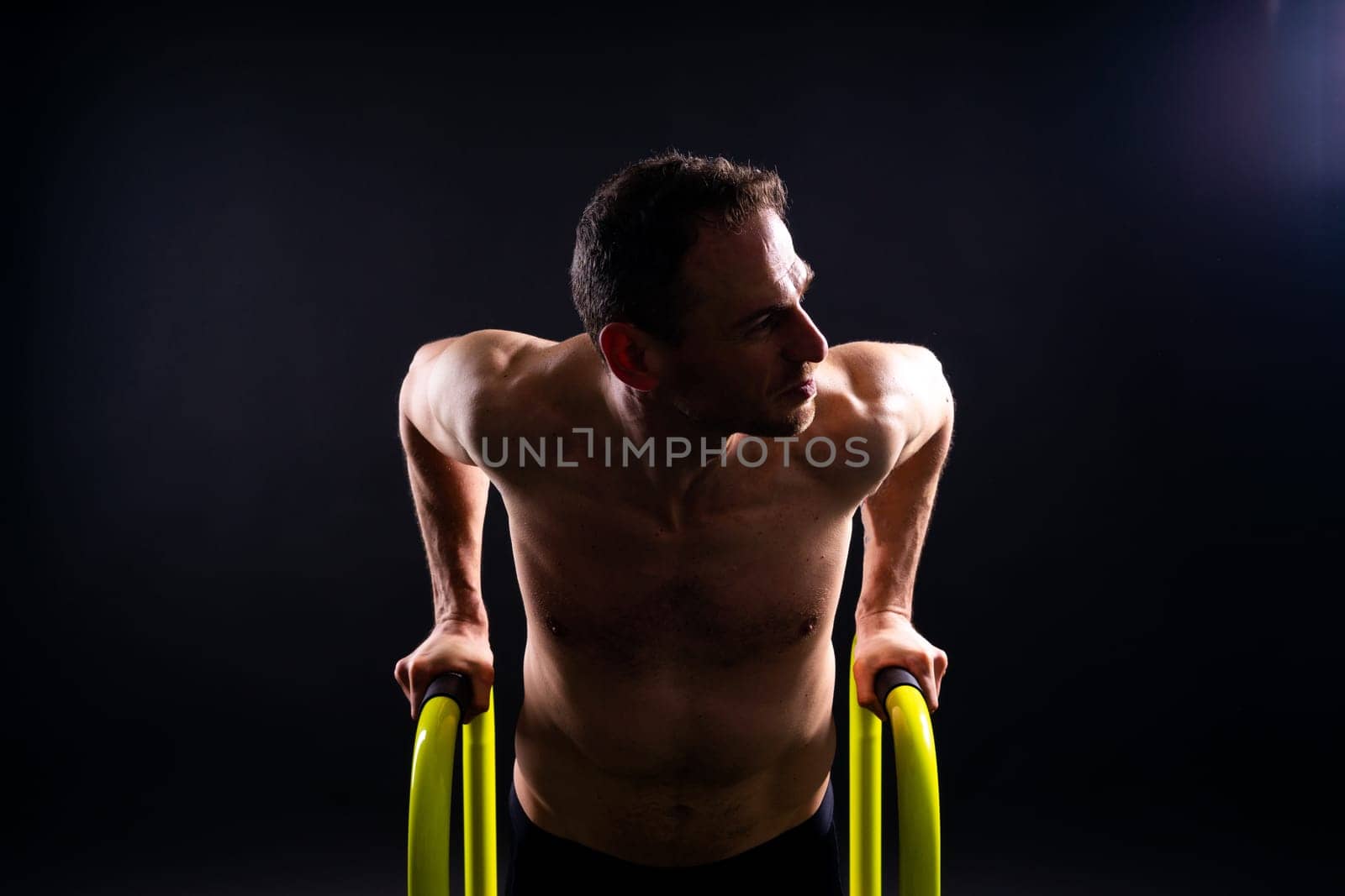 Front and side view photo of strong young man exercising on parallel bars in studio.