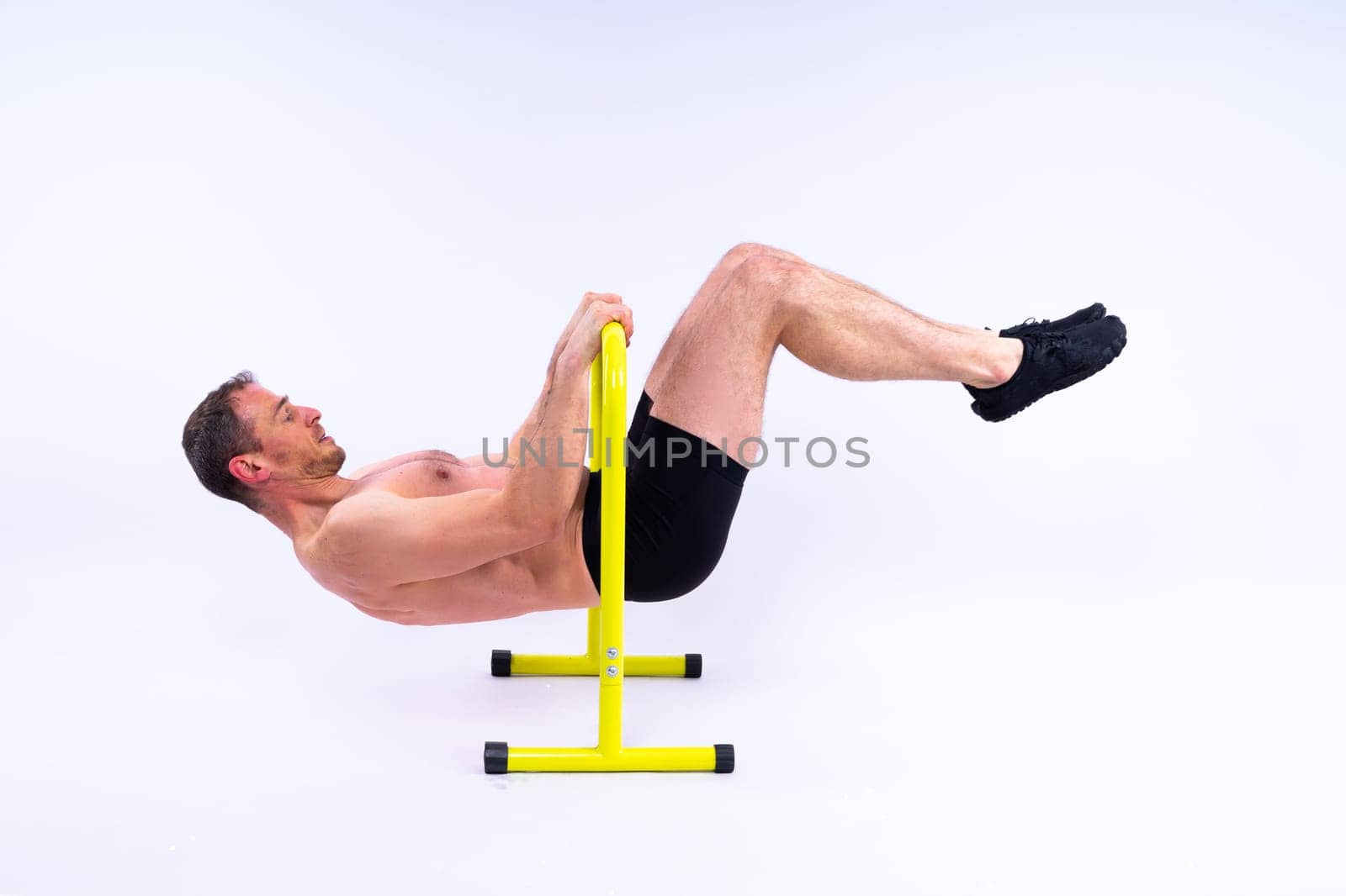 Front and side view photo of strong young man exercising on parallel bars in studio.