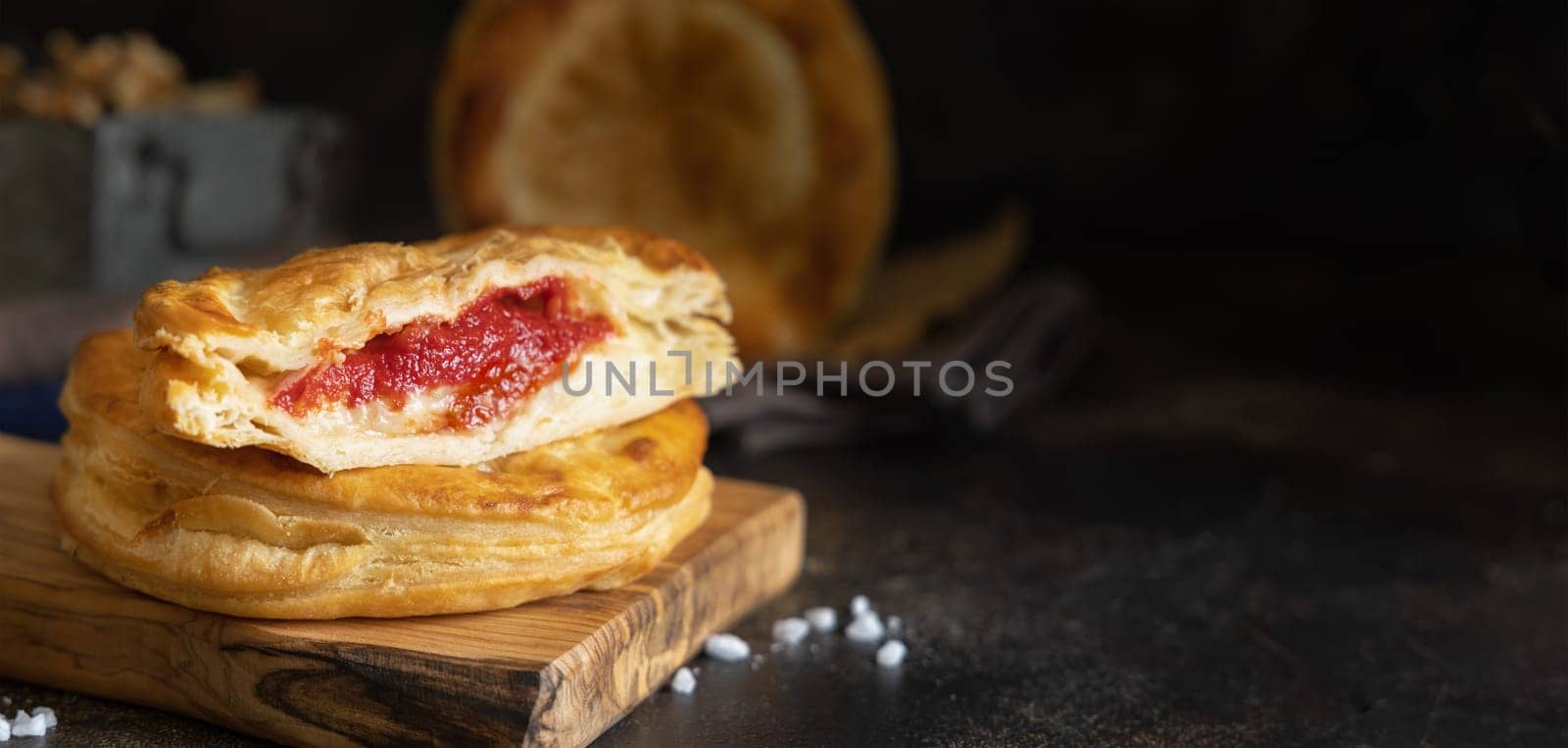 Rustico traditional puff pastry stuffed with bechamel sauce, tomato and mozzarella cheese, close up on a dark table, copy space. Traditional street food from Salento, Lecce, Italy