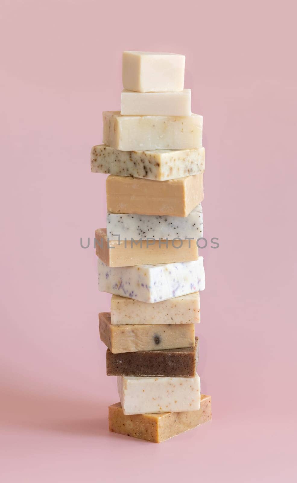 Tower stack of beige handmade soap bars on light pink close up. Natural herbal products for Spa and skin care