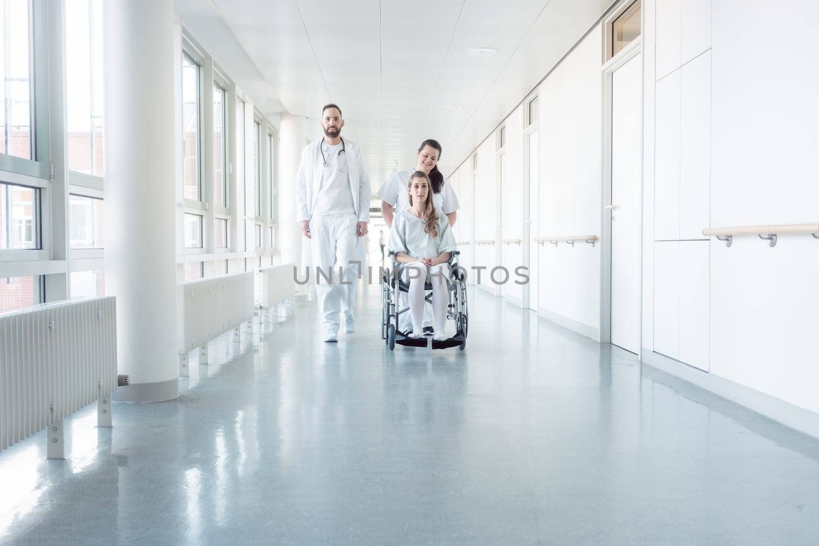 Doctor, nurse, and patient in wheelchair walking on hospital corridor