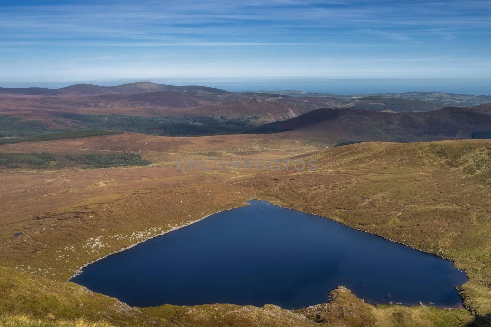 View from the top of Tonelagee mountain on heart shaped lake, Lough Ouler, reflecting blue sky. Hiking in Wicklow Mountains, Ireland