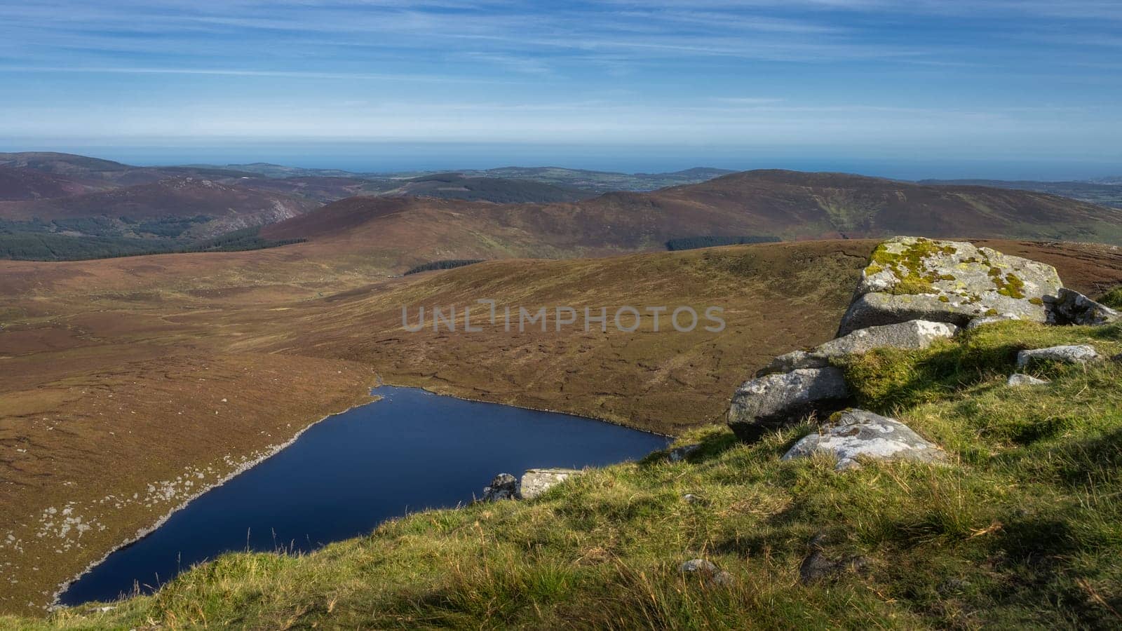 Stack of large rocks on a hillside of Tonelagee Mountain with a view on lake Lough Ouler, reflecting blue sky. Hiking in Wicklow Mountains, Ireland