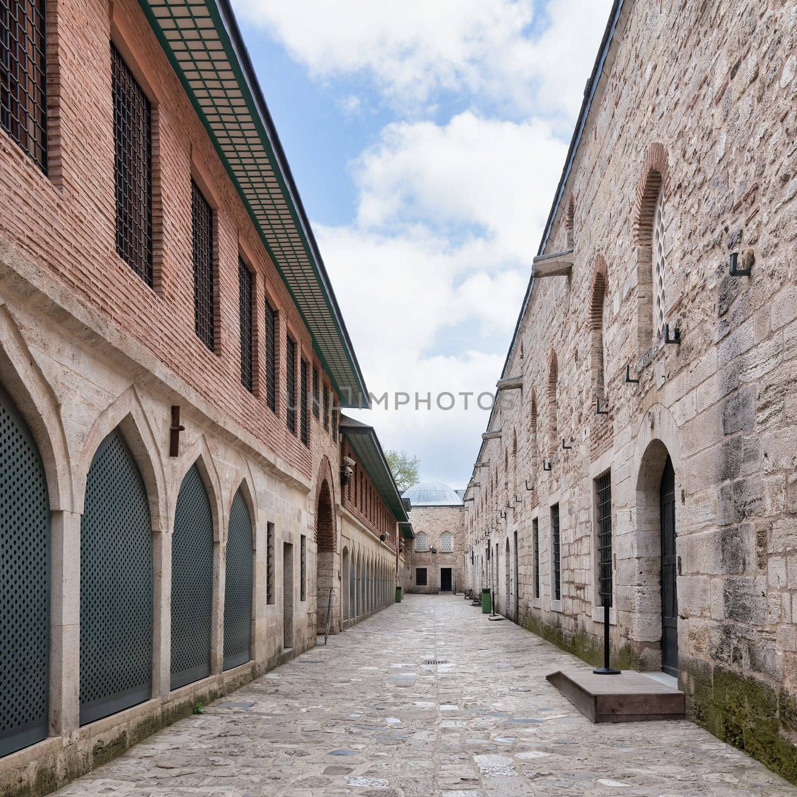 Paved walkway surrounded by aged stone brick walls with wrought iron windows in the courtyard of Topkapi palace, Istanbul, Turkey