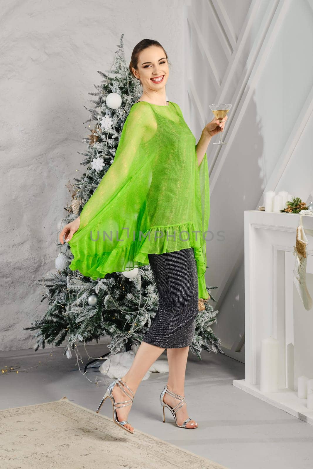 Glad and happy young woman spinning around herself with a glass of aperitif in hand near the Christmas tree