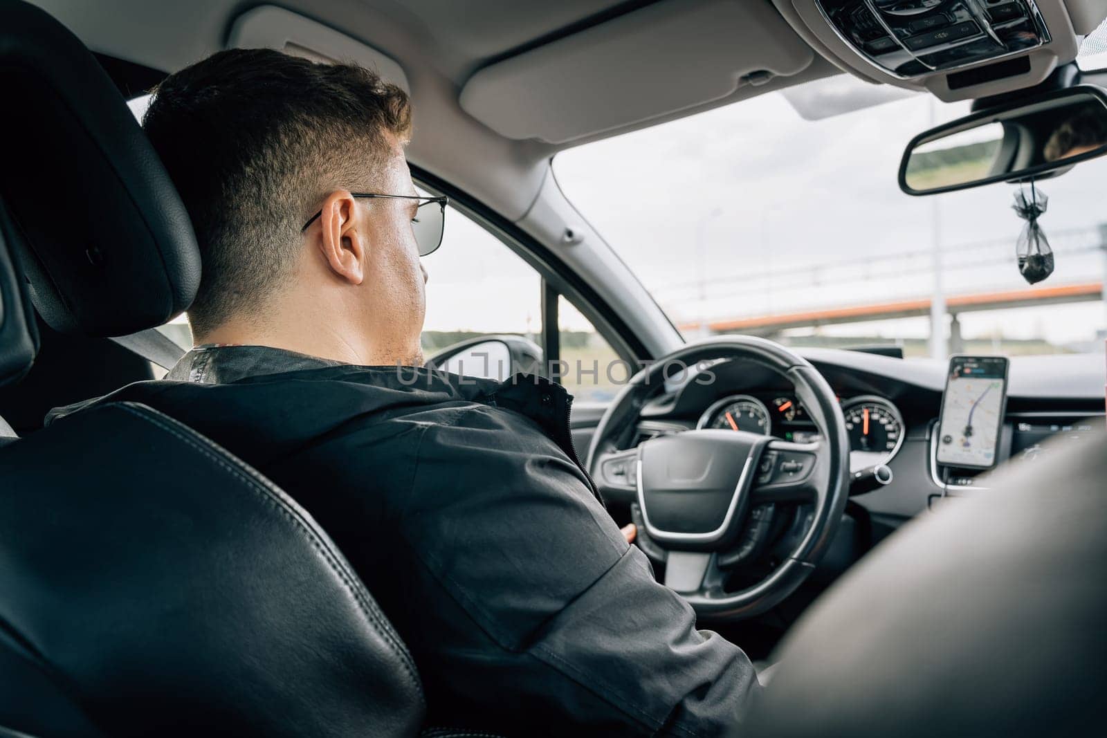 A man drives a car using a navigation application installed on a smartphone.