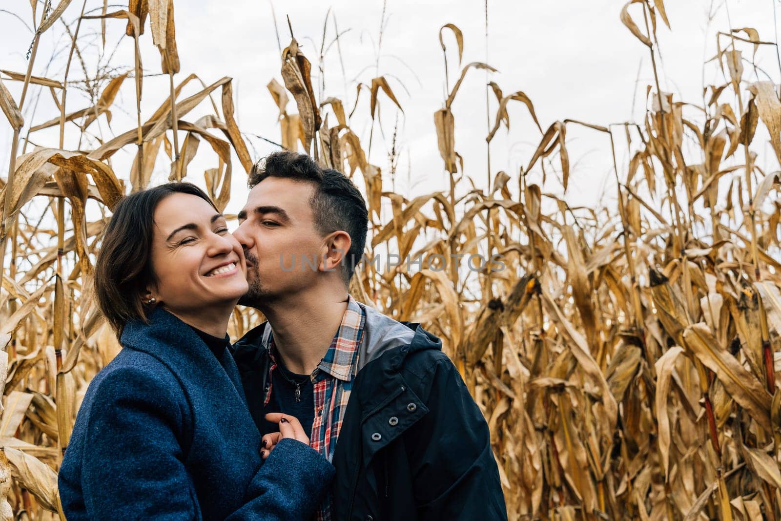 A man kisses a happy woman on the cheek while walking outside the city in a cornfield in autumn.