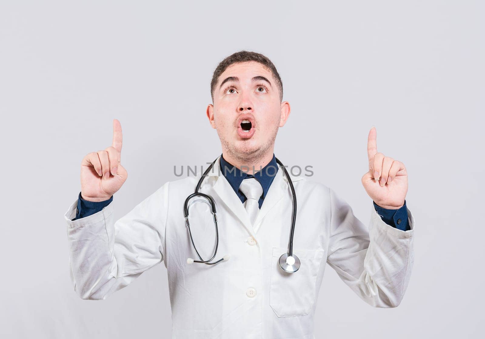 Amazed doctor pointing a promotion up. Male doctor looking and pointing up isolated, Surprised doctor pointing an advertisement up