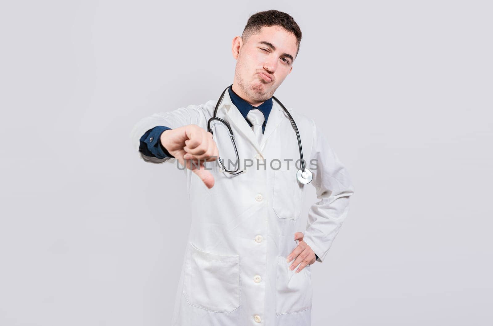 Doctor gesturing disapproval isolated. Unhappy doctor with thumb down isolated. Male doctor disapproving with fingers