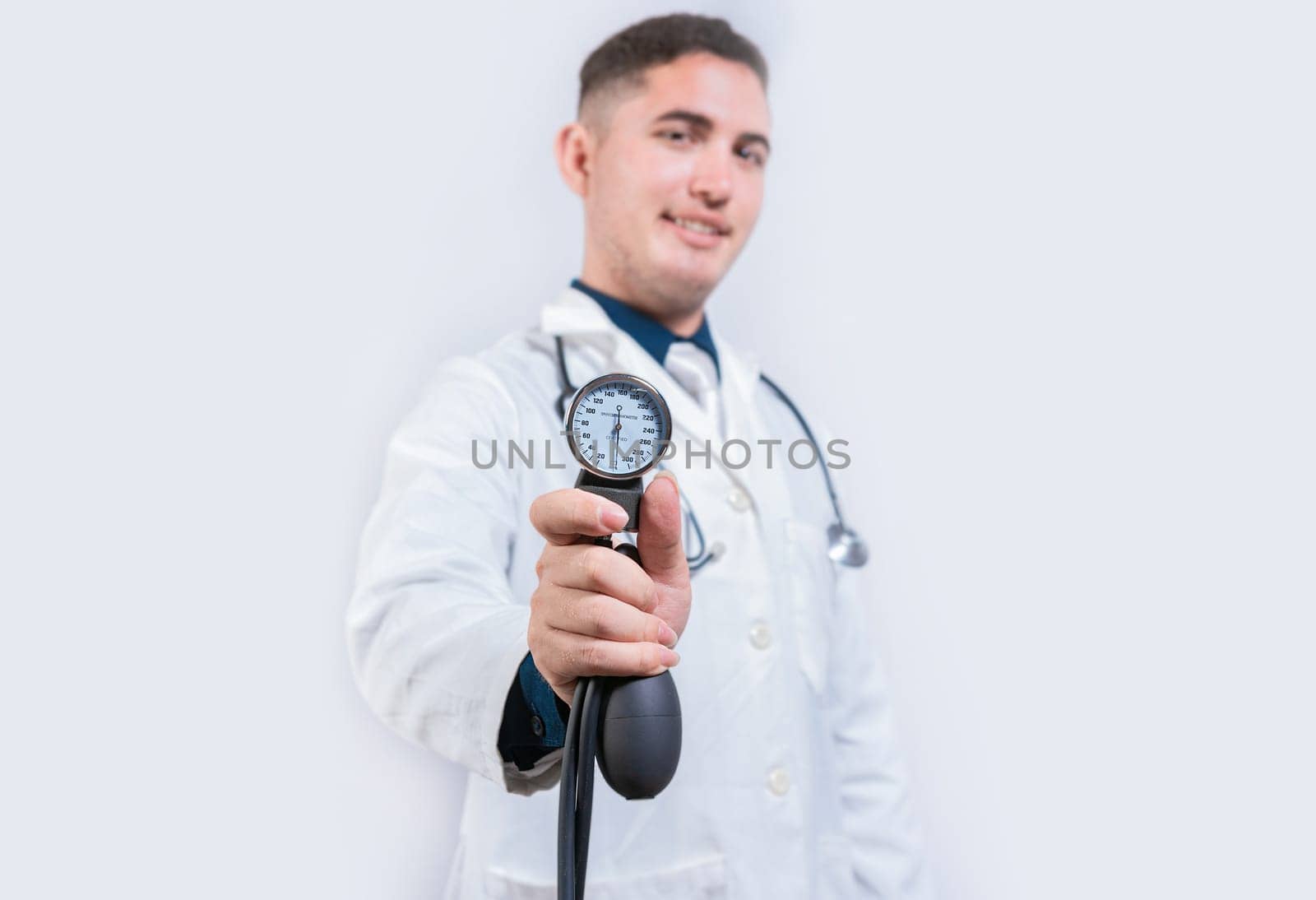 Latin doctor showing blood pressure monitor isolated. Young doctor holding tensiometer on isolated background