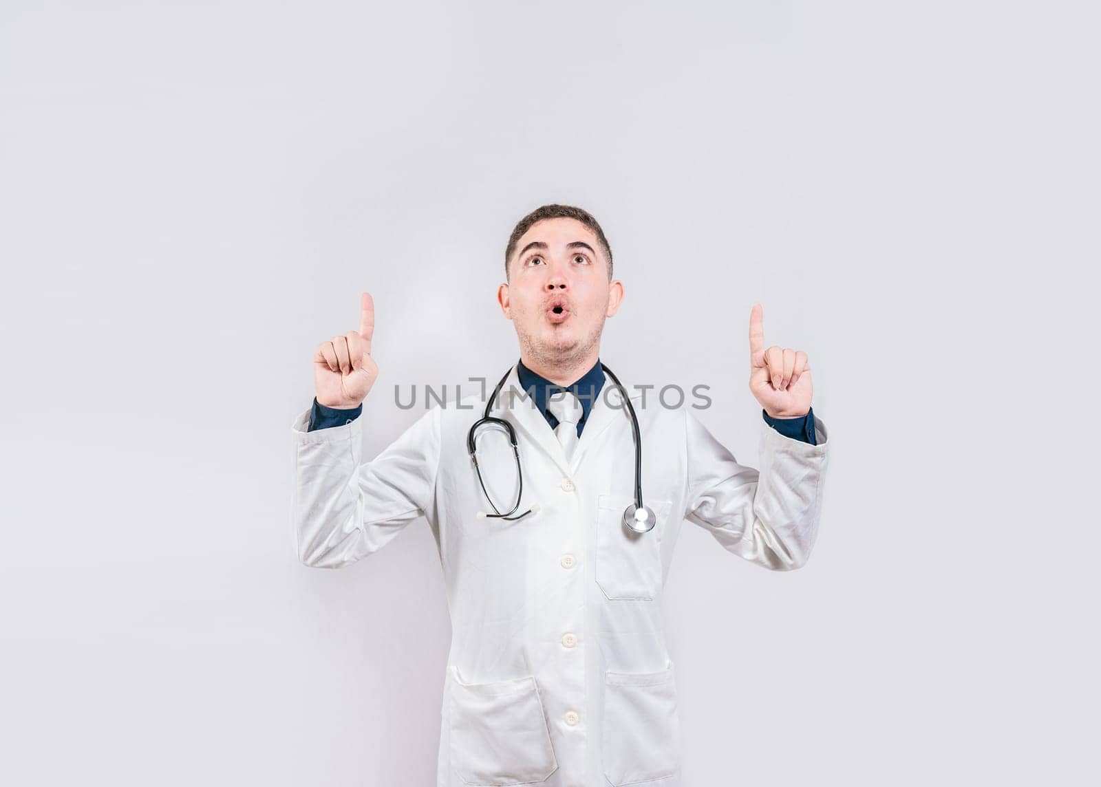 Surprised doctor pointing an advertisement up. Amazed doctor pointing a promotion up. Male doctor looking and pointing up isolated