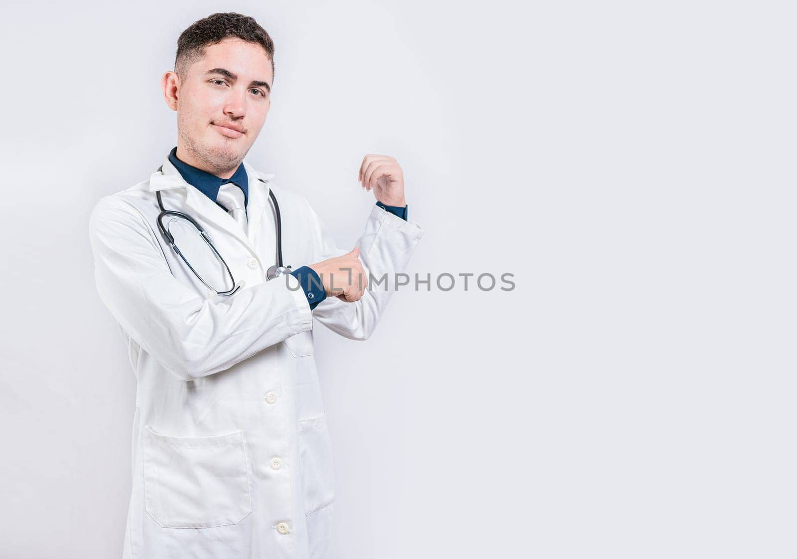 Doctor pointing back with his thumbs, recommending a product. Smiling latin doctor pointing back isolated