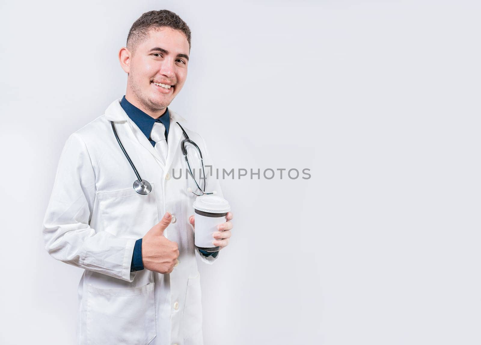 Satisfied doctor holding takeaway coffee isolated. Young doctor holding a coffee to go isolated. Smiling doctor holding coffee with thumb up