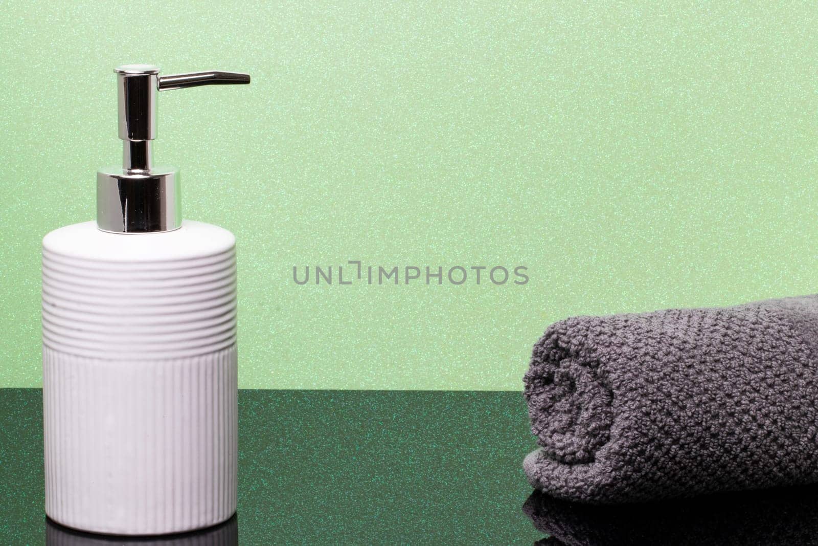 Macro of a beauty cosmetic makeup bottle and a fresh soft terry bath towel on dark table over green glittering background. Copy space for product display montage.