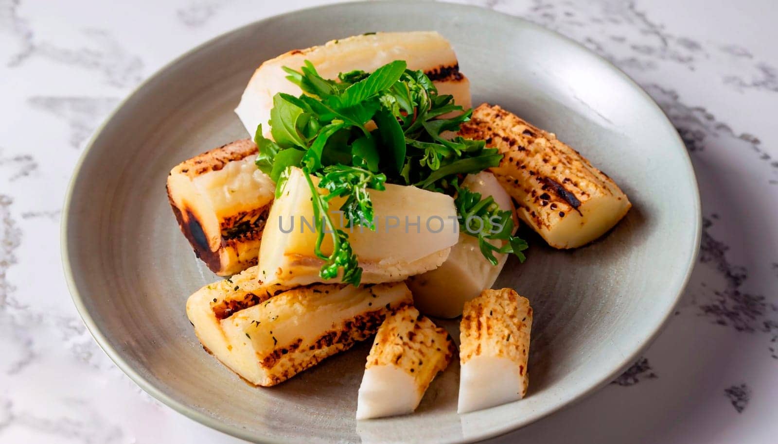 macro photo of cassava garnished with greens in a plate on a white marble serving table
