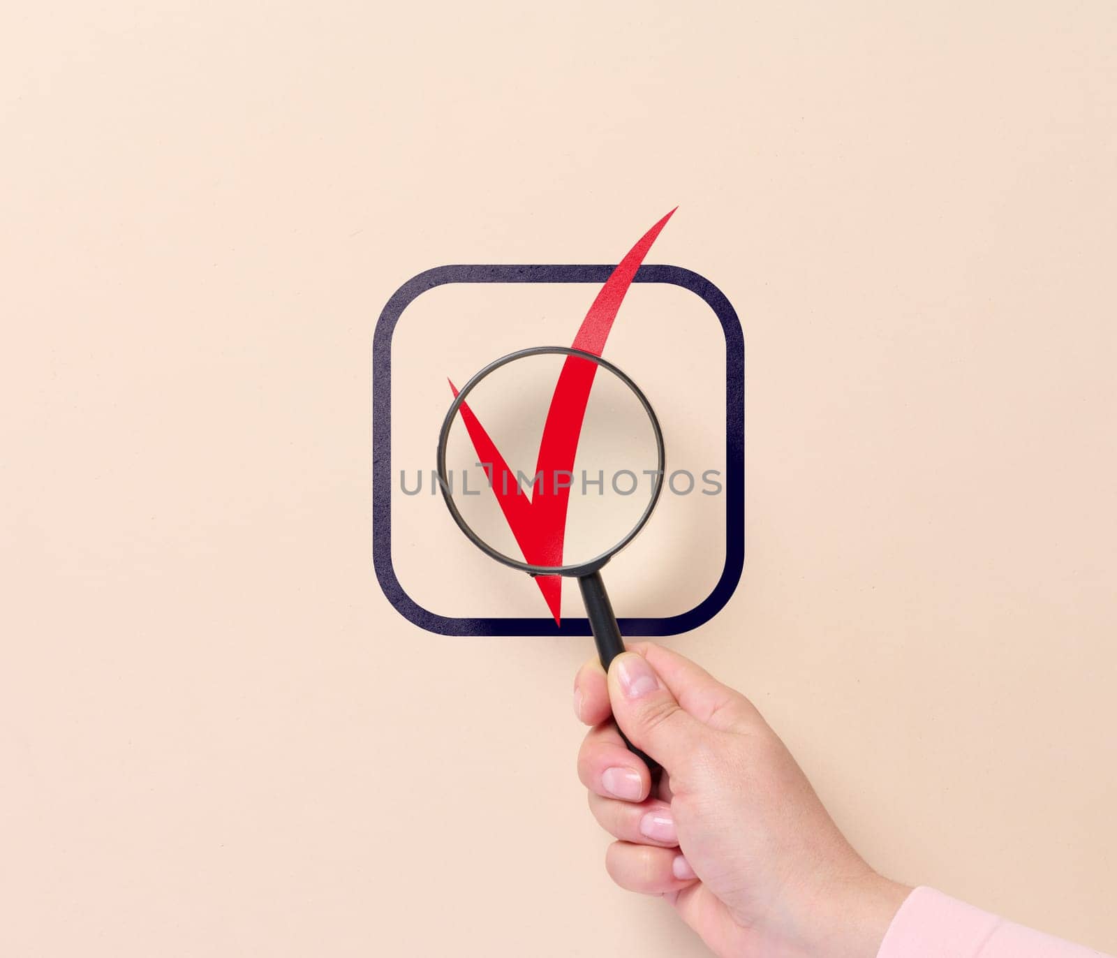 A hand holds a magnifying glass and a sign of approval in a cell. Business approval symbol, yes marks