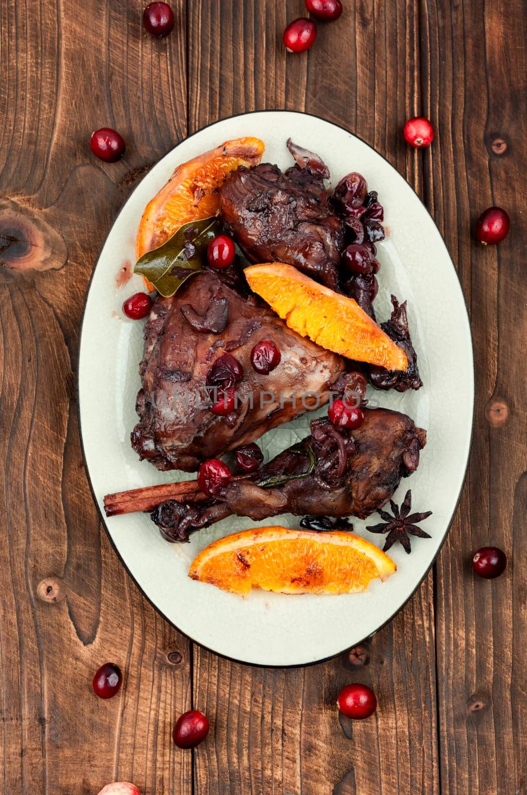 Chicken legs marinated in red wine, baked with orange and berries in white dish. Top view.