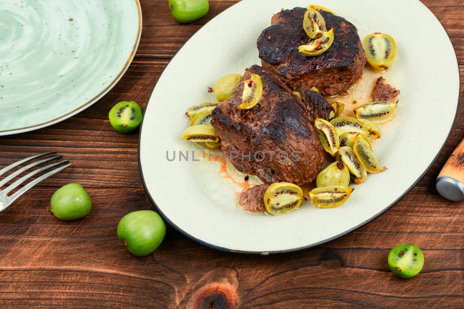 Dish of ostrich steak roasted with mini kiwi sauce. Meat with kiwi berries on wooden table.