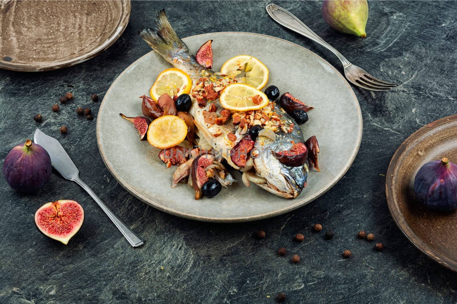 Baked gilt head bream, dorado fish with almonds and figs on rural wooden table. Autumn recipe.