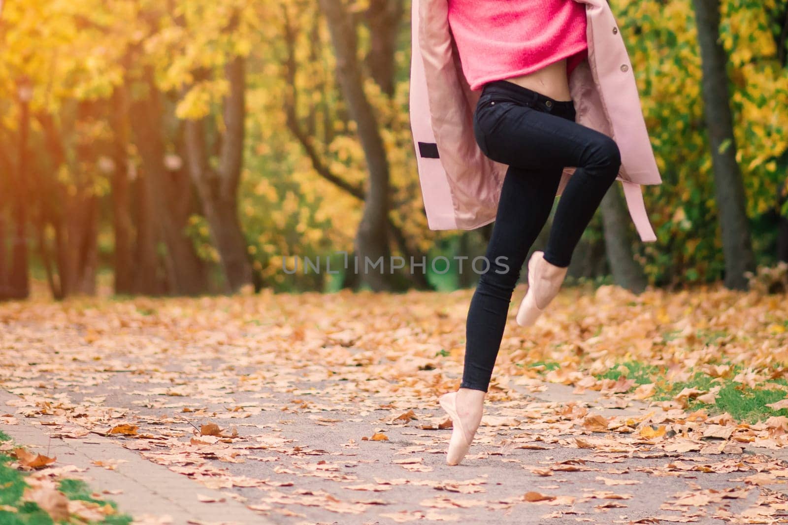 Woman ballerina dancing in pointe shoes in golden autumn park, standing in ballet pose on yellow leaves