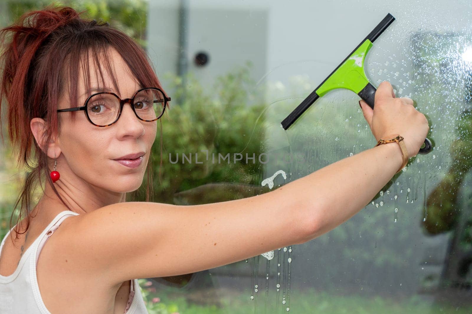 Beautiful young woman cleaning a window at home