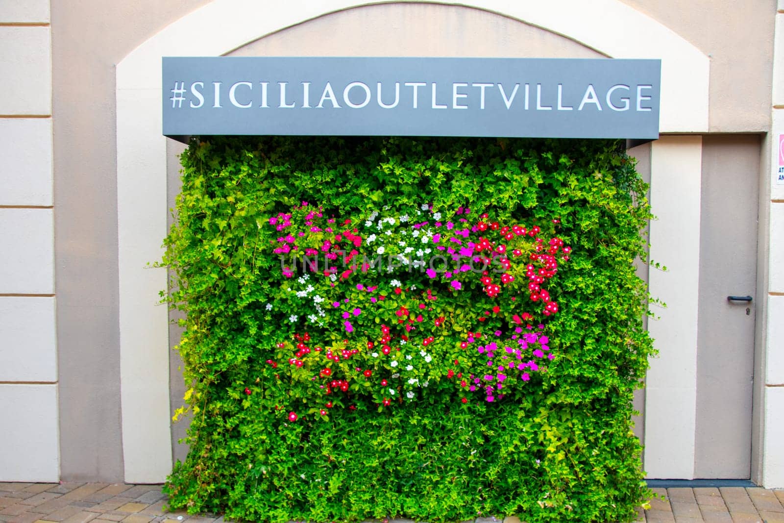 AGIRA, SICILY, Italy - 30 SEP 2023. Sicilia Outlet Village shopping centre is a popular visitor magnet for holidaymakers and locals alike. Flower advertisement wall.