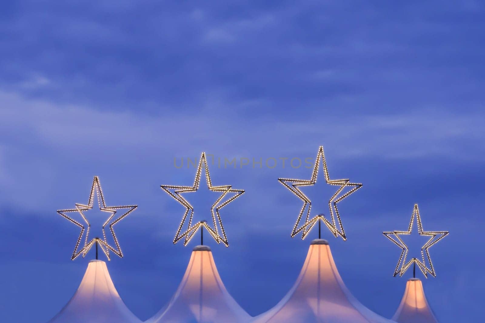 Wonderful x-mas season scene for visual or greetings card. Beautiful market tents with magic orange stars and blue sky at evening time.