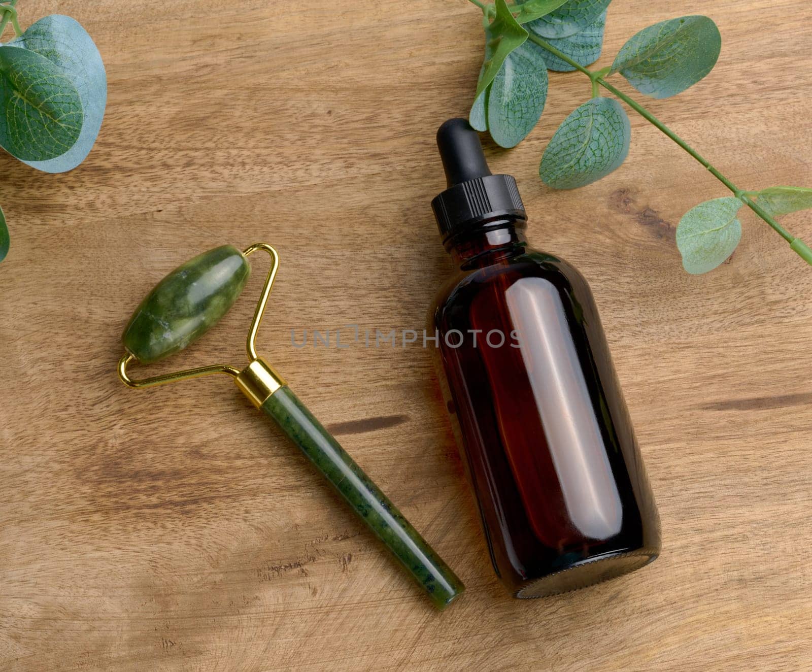 Brown glass bottle with a pipette,  stone hand massager for cosmetic procedures on a wooden background, top view