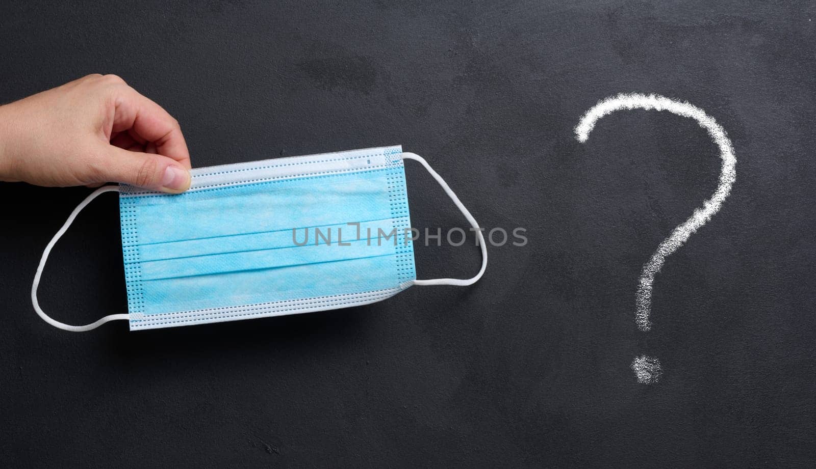 A woman's hand holds a disposable medical mask on a black chalk board background