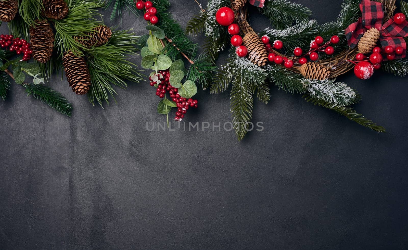 Branches and a round Christmas wreath made of fir branches and other decor on a black chalk board, space for an inscription