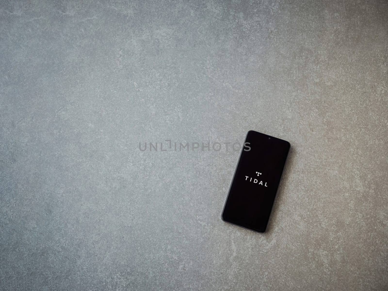 Lod, Israel - July 16,2023: TIDAL Music app launch screen on smartphone on ceramic stone background. Top view flat lay with copy space.