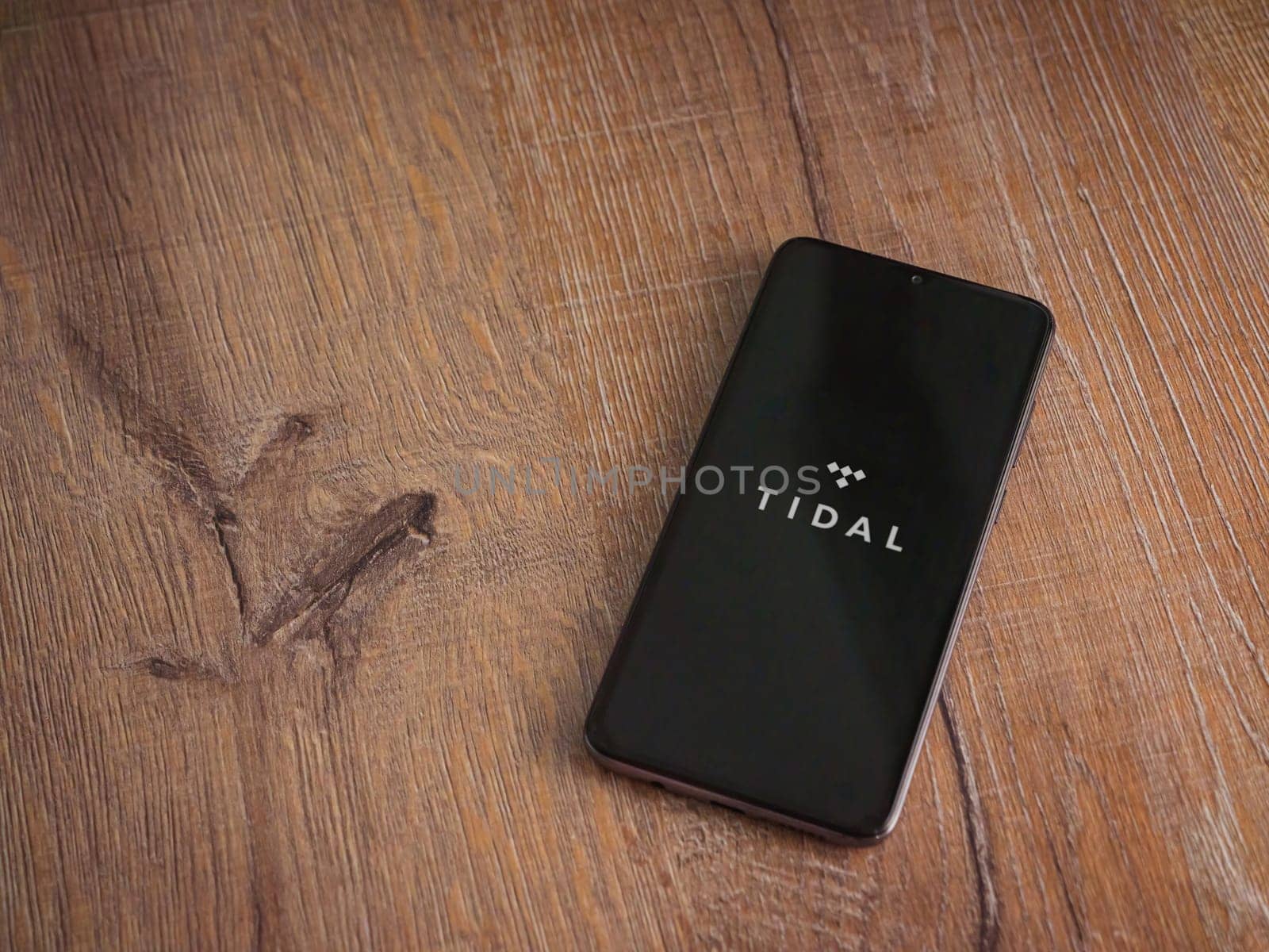 Lod, Israel - July 16,2023: TIDAL Music app launch screen on smartphone on wooden background. Top view flat lay with copy space.