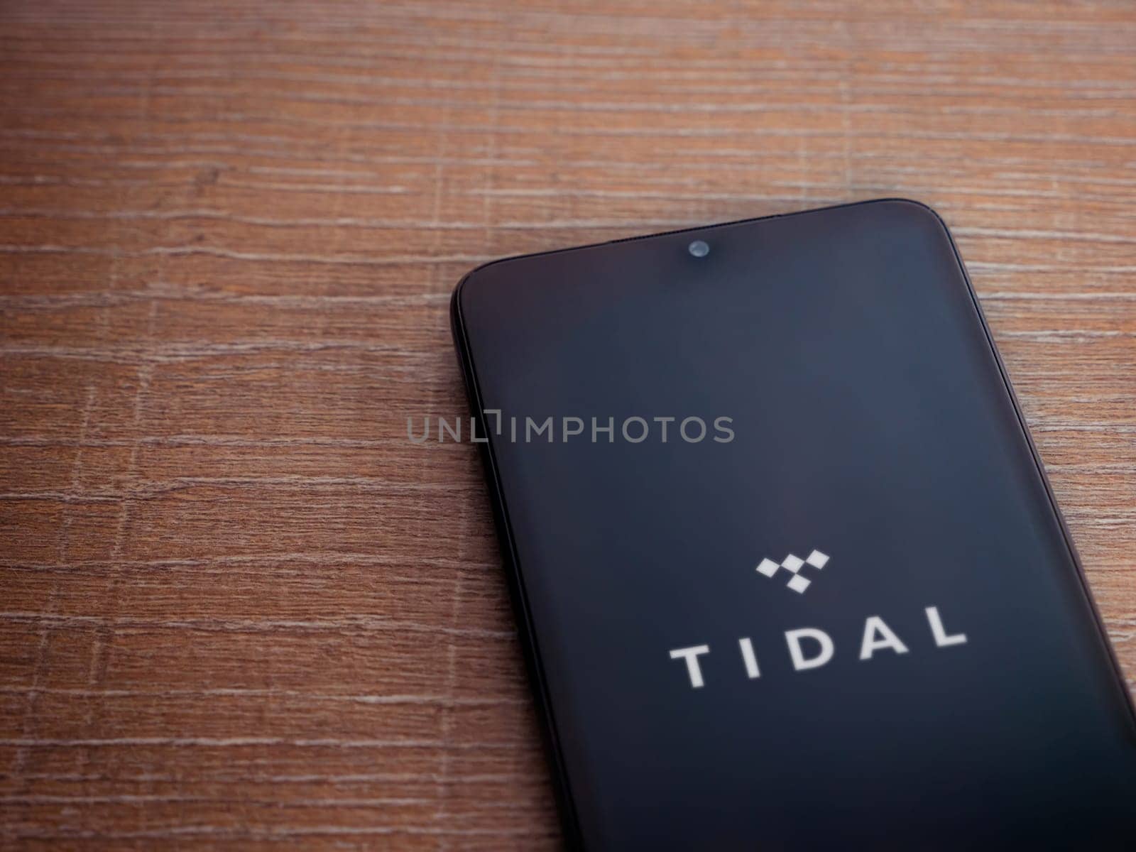 Lod, Israel - July 16,2023: TIDAL Music app launch screen on smartphone on wooden background. Top view flat lay with copy space.