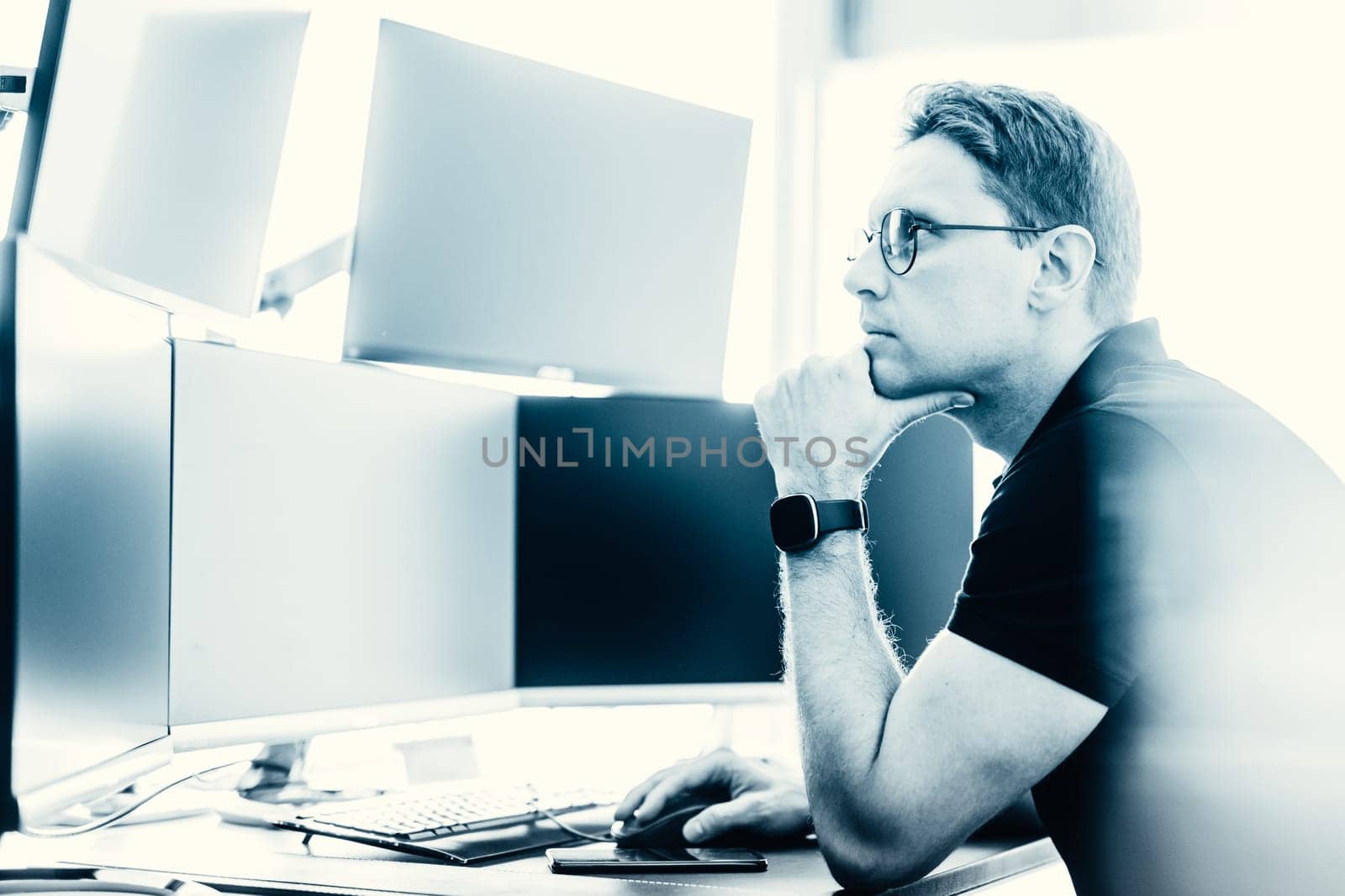 Male stock broker trading online watching charts and data analyses on multiple computer screens.