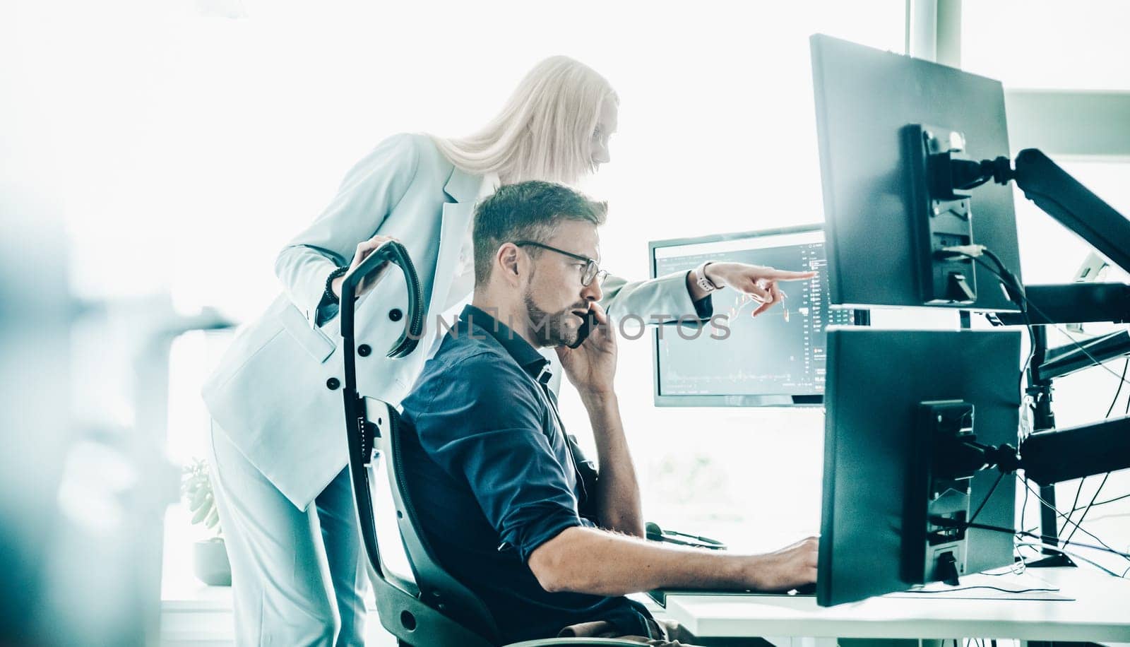 Stock broker business team trading online watching charts and data analyses on multiple computer screens in modern corporate work station office.