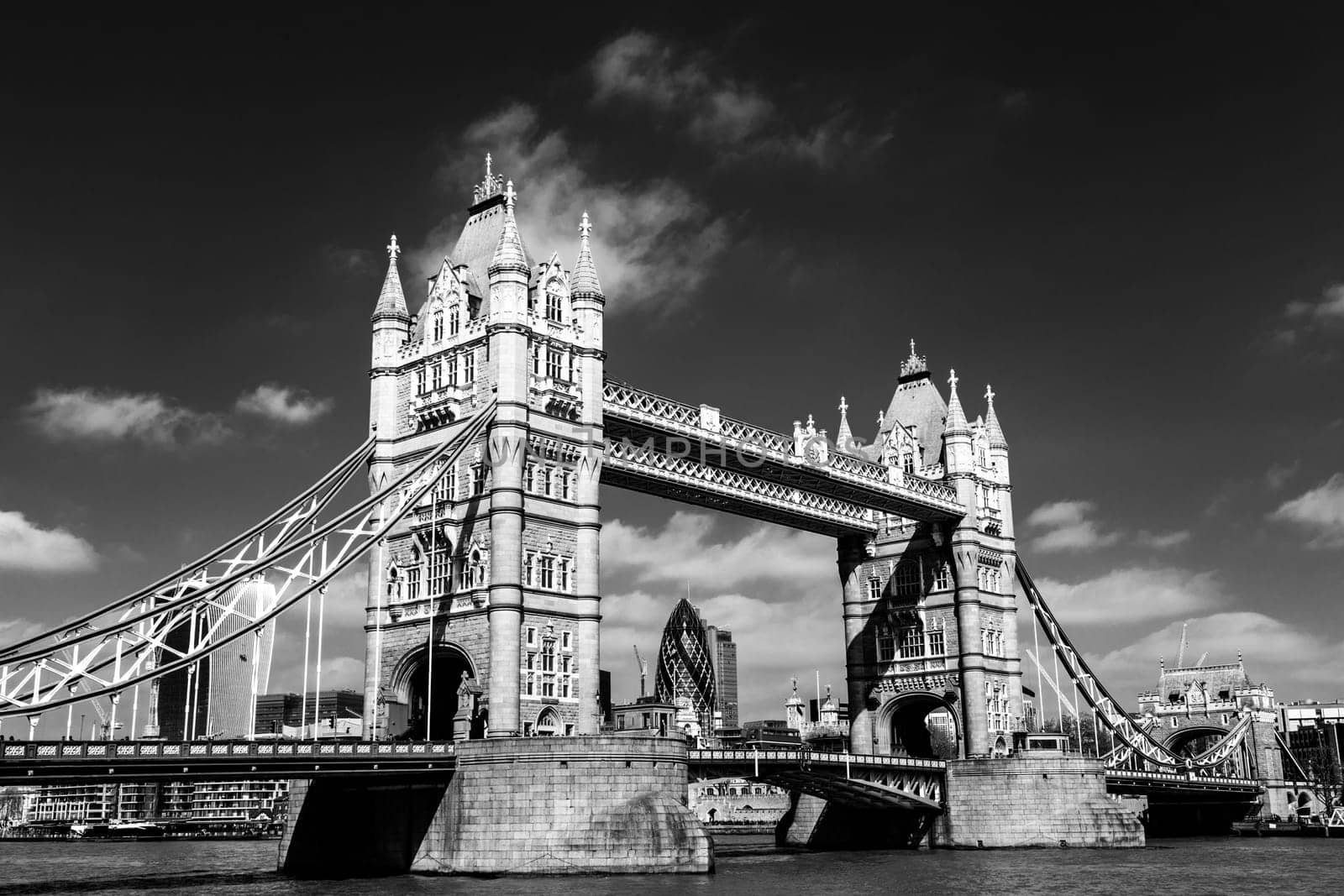 Red traditional double-decker bus driving on Tower Bridge in London, UK. London City skyscrapers in the background.
