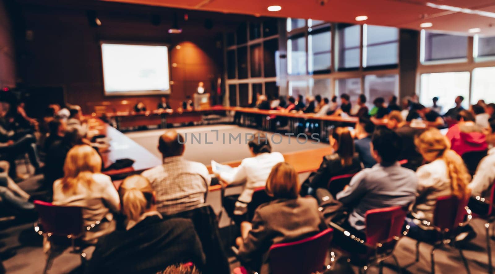Speaker giving a talk on corporate business event. Audience at the conference hall. Business and Entrepreneurship event. Focus on unrecognizable business people in the rear.