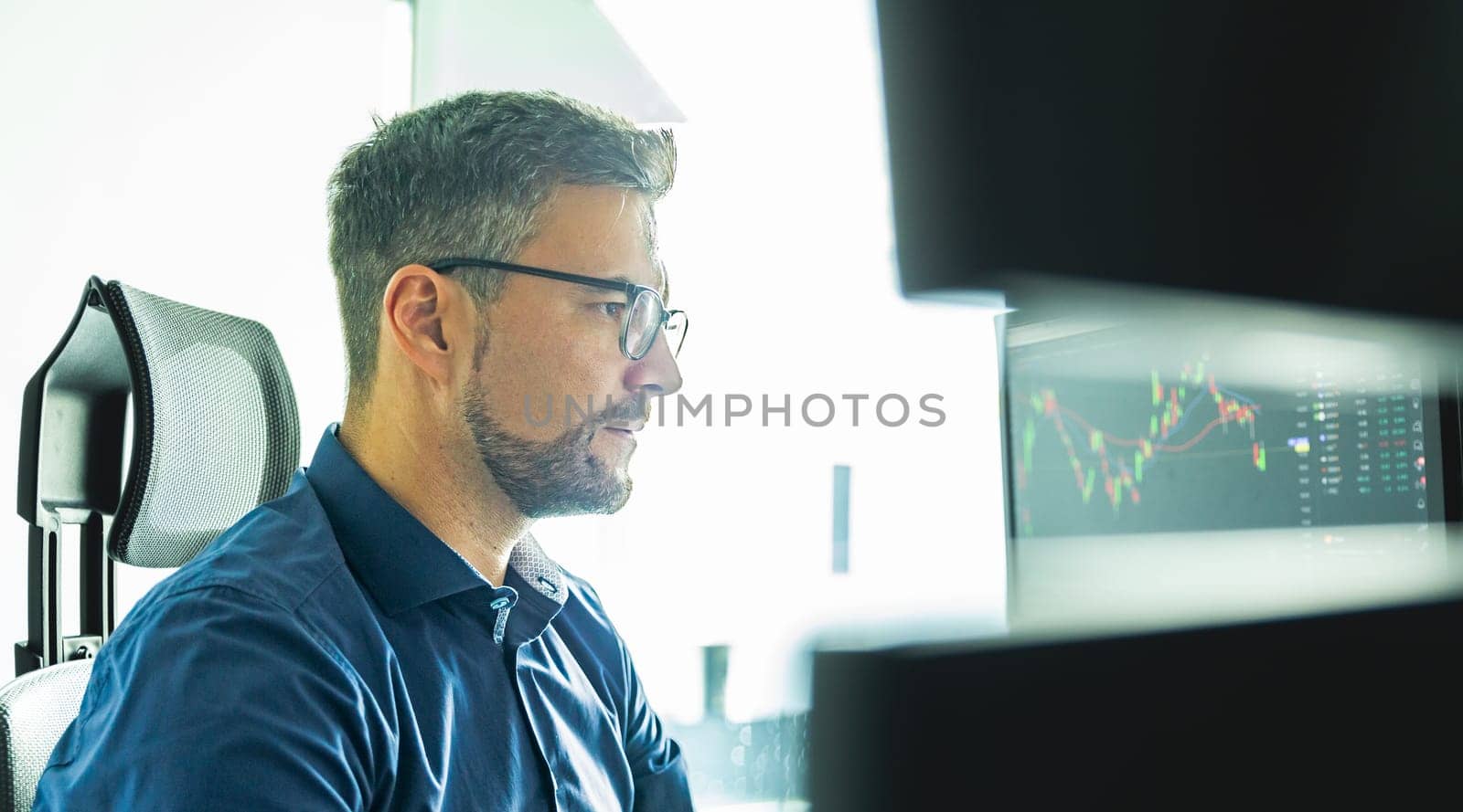 Male stock broker trading online watching charts and data analyses on multiple computer screens.