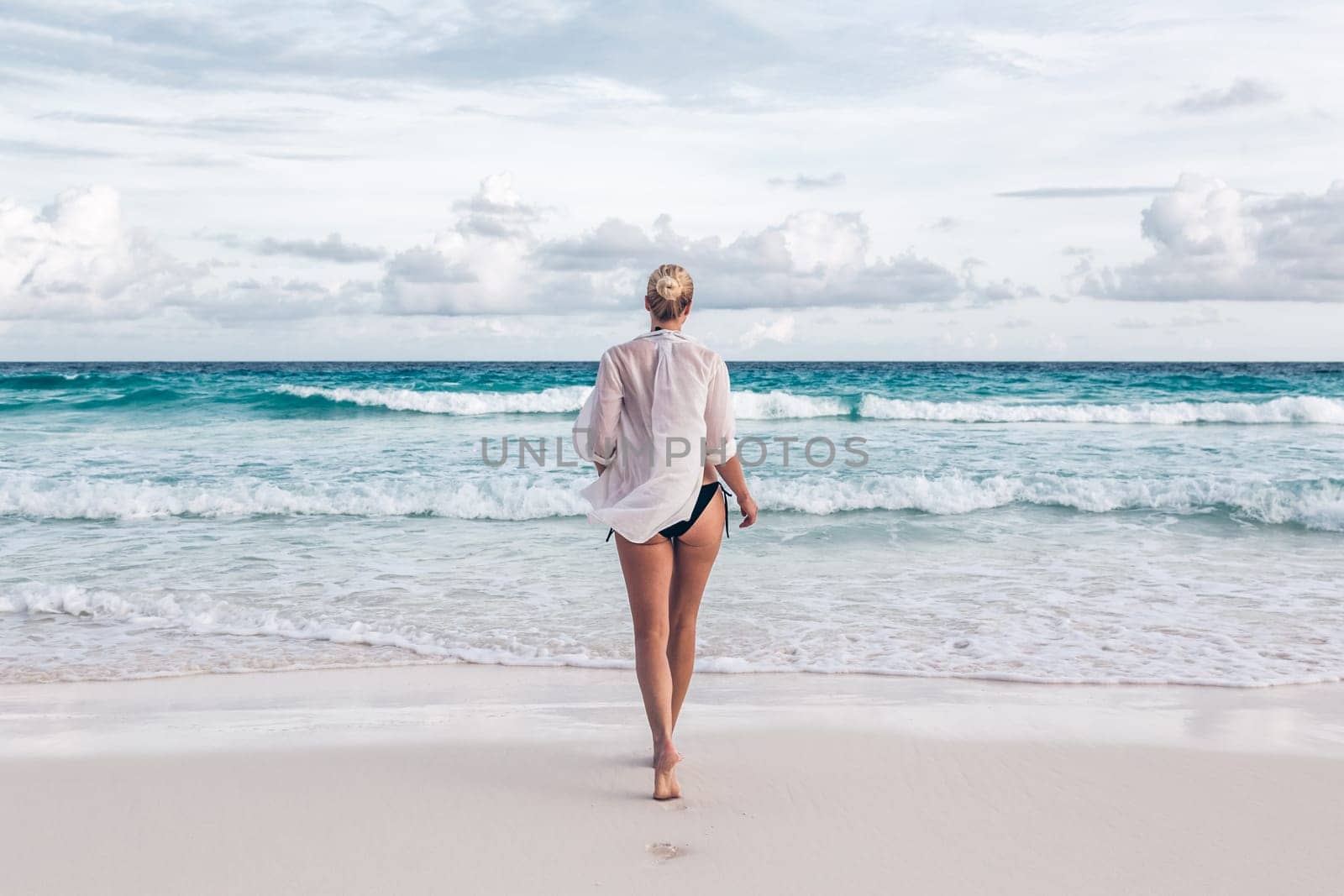 Woman wearing white loose tunic over bikini on Mahe Island, Seychelles. Summer vacations on picture perfect tropical beach concept.